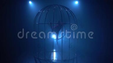 空中体操运动员在舞台上笼中篮圈上的舞台表演。 蓝色烟雾背景。 剪影。 慢动作